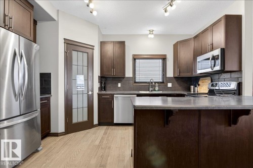 The kitchen features wood cabinetry, light-colored flooring, and stainless steel appliances, including a refrigerator, microwave, and dishwasher - 1530 Chapman Way, Edmonton, AB - Indoor Photo Showing Kitchen With Stainless Steel Kitchen