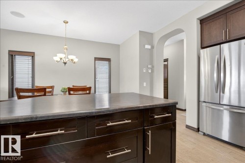 The kitchen features a dark wood island with a solid surface countertop, stainless steel refrigerator, and dark wood cabinetry - 1530 Chapman Way, Edmonton, AB - Indoor Photo Showing Kitchen