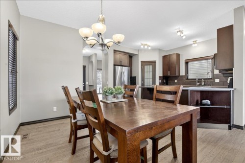 Dining area featuring hardwood floors and a chandelier, with a view of the kitchen which includes dark wood cabinetry, a window with blinds, and a stainless steel sink - 1530 Chapman Way, Edmonton, AB - Indoor Photo Showing Dining Room