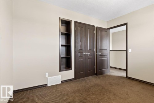 This room features warm neutral-toned walls, brown carpet, and a built-in shelving unit - 1530 Chapman Way, Edmonton, AB - Indoor Photo Showing Other Room