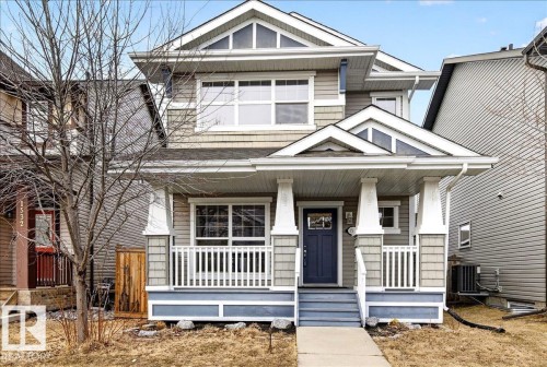 The property features a charming front porch with white railings and columns, a dark blue front door with an ornate glass insert, and a light grey exterior with shingle and horizontal siding details - 1530 Chapman Way, Edmonton, AB - Outdoor With Deck Patio Veranda With Facade