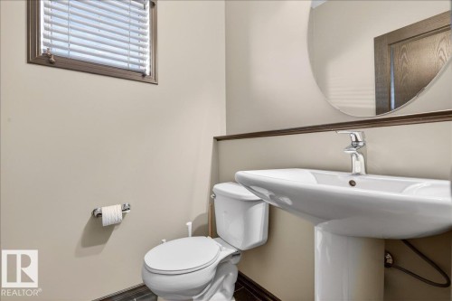 Bathroom featuring a pedestal sink with a chrome faucet, a round mirror, and a window with blinds - 1530 Chapman Way, Edmonton, AB - Indoor Photo Showing Bathroom