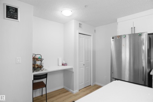 The kitchen features a stainless steel refrigerator, white cabinetry with dark handles, and light wood flooring - 103 3353 16A Avenue, Edmonton, AB - Indoor