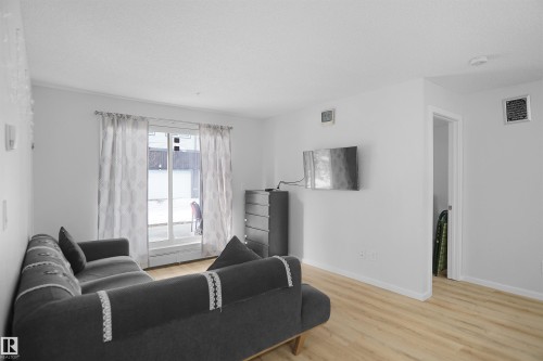 Living room featuring light-toned flooring, white walls, and a sliding glass door providing outdoor access - 103 3353 16A Avenue, Edmonton, AB - Indoor Photo Showing Living Room