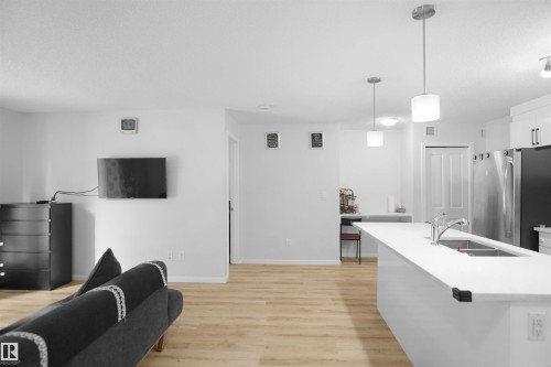 Open concept living area featuring light wood flooring, a kitchen island with a sink, and stainless steel appliances - 103 3353 16A Avenue, Edmonton, AB - Indoor Photo Showing Kitchen With Double Sink