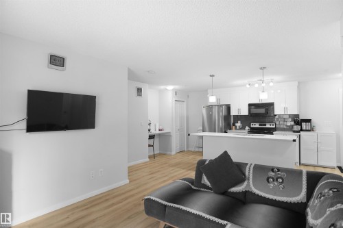 Open concept living area with light-toned flooring and a kitchen featuring white cabinetry, a kitchen island, and stainless steel appliances - 103 3353 16A Avenue, Edmonton, AB - Indoor