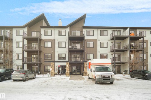 The property features a modern multi-story exterior with a mix of light and dark siding, accented by stone pillars at the entrance - 103 3353 16A Avenue, Edmonton, AB - Outdoor With Facade