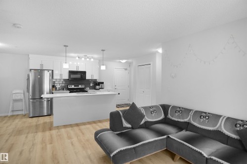 The open concept design integrates the living area with a contemporary kitchen, featuring light-toned flooring throughout - 103 3353 16A Avenue, Edmonton, AB - Indoor Photo Showing Kitchen