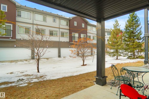 The property features a patio with an overhead structure, offering a view of the surrounding landscape with mature evergreen trees and a multi-level building - 103 3353 16A Avenue, Edmonton, AB - Outdoor