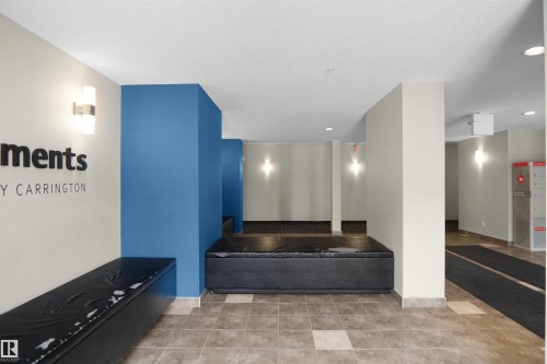 The property features a common area with tiled flooring, wall-mounted light fixtures, and a blue accent wall - 103 3353 16A Avenue, Edmonton, AB - Indoor Photo Showing Other Room
