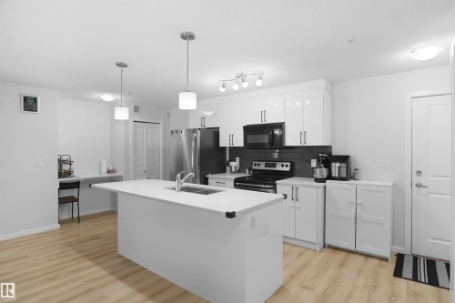The kitchen features a central island with a sink, white cabinetry, and stainless steel appliances - 103 3353 16A Avenue, Edmonton, AB - Indoor Photo Showing Kitchen With Double Sink With Upgraded Kitchen