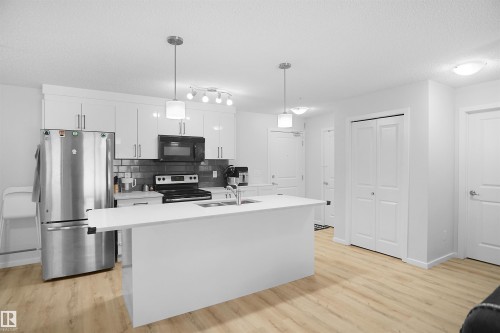 Modern kitchen featuring white cabinetry, stainless steel appliances, a white island with an integrated sink, and light wood-tone flooring - 103 3353 16A Avenue, Edmonton, AB - Indoor Photo Showing Kitchen With Double Sink With Upgraded Kitchen