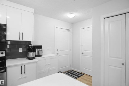 The kitchen features white cabinetry with black hardware, a dark subway tile backsplash, and white countertops - 103 3353 16A Avenue, Edmonton, AB - Indoor Photo Showing Other Room