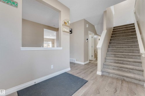 The entrance features light wood-style flooring, a carpeted staircase with white railings, and a wall cutout providing a view into an interior area - 121 64 Street, Edmonton, AB - Indoor Photo Showing Other Room