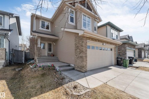 The property features a two-story exterior with siding and brick accents, a front entry with a small porch, and an attached garage with a driveway - 121 64 Street, Edmonton, AB - Outdoor