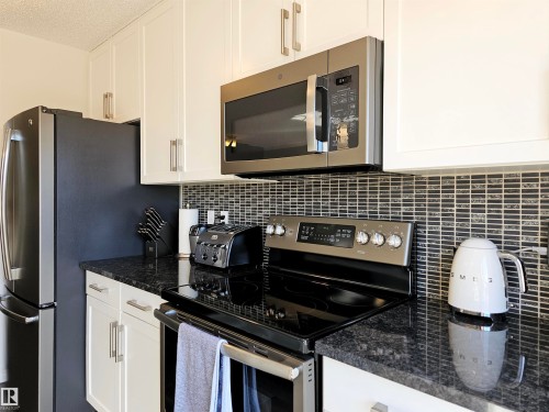 The kitchen features white cabinetry, dark countertops, a tile backsplash, and stainless steel appliances including a refrigerator, microwave, and range - 6888 Evans Wynd, Edmonton, AB - Indoor Photo Showing Kitchen With Stainless Steel Kitchen With Upgraded Kitchen