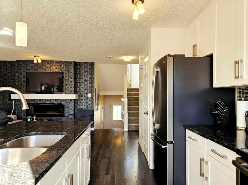 The property features a kitchen with dark granite countertops, white cabinetry, and stainless steel appliances - 6888 Evans Wynd, Edmonton, AB - Indoor Photo Showing Kitchen With Double Sink