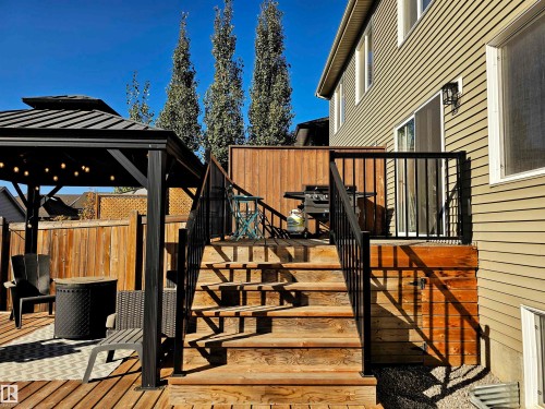 The property features a multi-level wooden deck with black railings, a wooden privacy fence, and a gazebo with overhead lighting - 6888 Evans Wynd, Edmonton, AB - Outdoor With Deck Patio Veranda With Exterior