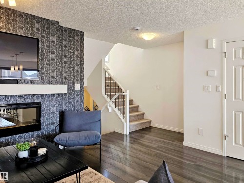 Living area featuring dark wood floors, a fireplace with a decorative surround, and a staircase with a white railing and dark balusters - 6888 Evans Wynd, Edmonton, AB - Indoor Photo Showing Other Room With Fireplace
