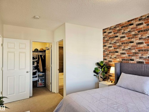 Bedroom featuring a decorative brick-style accent wall, carpeted flooring, and a closet with shelving - 6888 Evans Wynd, Edmonton, AB - Indoor Photo Showing Bedroom