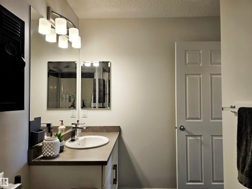 Bathroom featuring a vanity with an oval sink, a wall-mounted light fixture, and a mirrored wall - 6888 Evans Wynd, Edmonton, AB - Indoor Photo Showing Bathroom