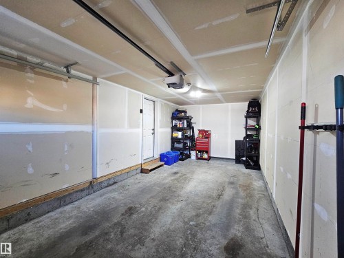 The property includes a spacious garage with a concrete floor, a white utility door, and overhead lighting - 6888 Evans Wynd, Edmonton, AB - Indoor Photo Showing Garage