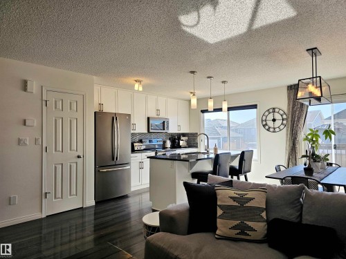 The open concept living area features dark hardwood flooring and a kitchen with white cabinetry, dark countertops, and stainless steel appliances - 6888 Evans Wynd, Edmonton, AB - Indoor Photo Showing Kitchen With Stainless Steel Kitchen