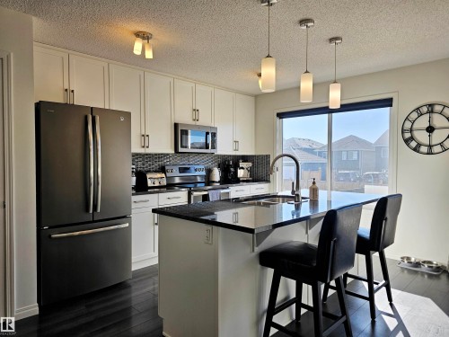 Well-appointed kitchen featuring a large window, dark wood floors, white cabinetry, and stainless steel appliances - 6888 Evans Wynd, Edmonton, AB - Indoor Photo Showing Kitchen With Stainless Steel Kitchen With Upgraded Kitchen