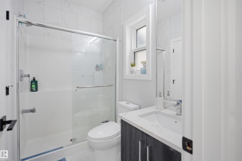Well-appointed bathroom featuring a shower with a glass enclosure, a window providing natural light, and a vanity with a white countertop and dark cabinetry - 2420 13 Avenue, Edmonton, AB - Indoor Photo Showing Bathroom