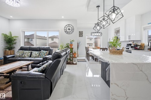 Open concept living area with white tile flooring throughout, featuring a kitchen island with a marble-like countertop, a dining area with a table and chairs, and a living area with a large window - 2420 13 Avenue, Edmonton, AB - Indoor