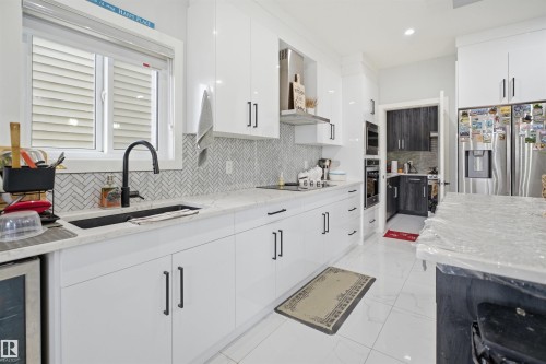The kitchen features white cabinetry, a herringbone tile backsplash, a stainless steel refrigerator, and a built-in oven and microwave - 2420 13 Avenue, Edmonton, AB - Indoor Photo Showing Kitchen With Upgraded Kitchen