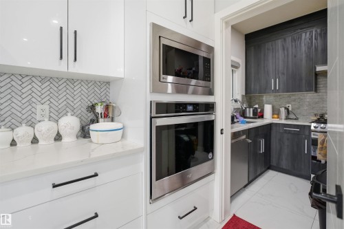 Kitchen featuring white cabinetry with black hardware, a stainless steel microwave and oven, and a white herringbone tile backsplash - 2420 13 Avenue, Edmonton, AB - Indoor Photo Showing Kitchen