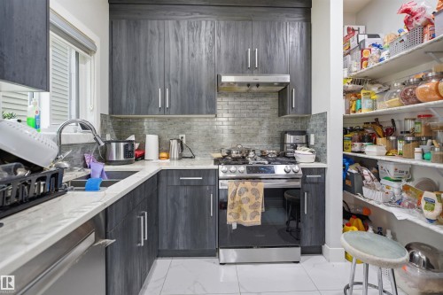 The kitchen features grey wood-grain cabinetry, stainless steel appliances, a white marble-patterned countertop, and a tiled backsplash - 2420 13 Avenue, Edmonton, AB - Indoor Photo Showing Kitchen With Double Sink