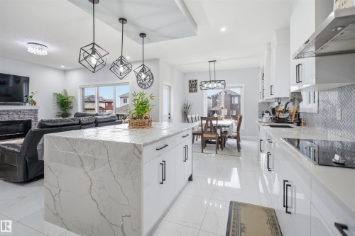 The kitchen showcases a central island with a light-colored countertop, white cabinetry with black handles, and a herringbone pattern backsplash - 2420 13 Avenue, Edmonton, AB - Indoor Photo Showing Kitchen With Upgraded Kitchen