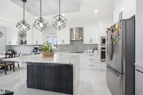 Contemporary kitchen featuring white cabinetry, a large island with a light-colored countertop, stainless steel appliances, and geometric pendant lighting - 2420 13 Avenue, Edmonton, AB - Indoor Photo Showing Kitchen With Upgraded Kitchen