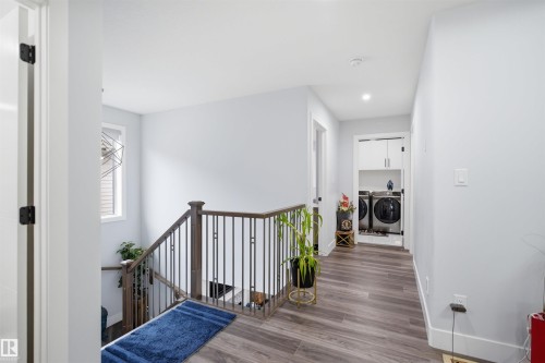 The property features modern wood-style flooring, a staircase with dark wood handrails and black metal spindles, and a dedicated laundry area with washer, dryer, and white cabinetry - 2420 13 Avenue, Edmonton, AB - Indoor Photo Showing Other Room