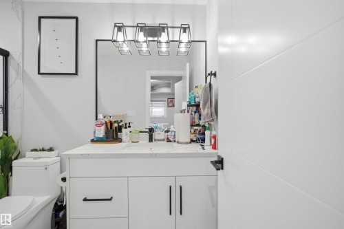Bathroom featuring a vanity with a white countertop and dark fixtures, a dark-framed mirror, and contemporary lighting - 2420 13 Avenue, Edmonton, AB - Indoor Photo Showing Bathroom