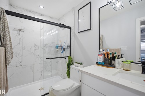 Bathroom featuring a glass-enclosed shower with white marble-style tiled walls, a white vanity with a white countertop, and a large mirror - 2420 13 Avenue, Edmonton, AB - Indoor Photo Showing Bathroom