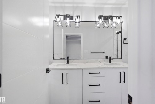 The bathroom features a double vanity with white cabinetry, a light-colored countertop, and a large mirror framed in black - 2420 13 Avenue, Edmonton, AB - 