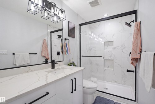 This bathroom features a contemporary vanity with a white countertop and black fixtures, a spacious walk-in shower with white marbled tiles, and a modern shower head - 2420 13 Avenue, Edmonton, AB - Indoor Photo Showing Bathroom