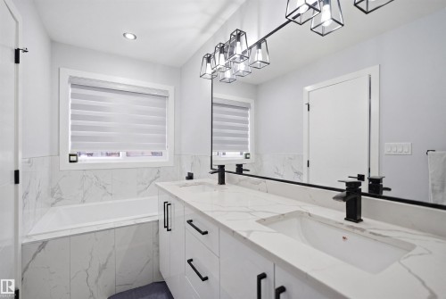 Well-appointed bathroom featuring a double vanity with stone countertops and undermount sinks, a large mirror, and a bathtub with tiled surround - 2420 13 Avenue, Edmonton, AB - Indoor Photo Showing Other Room