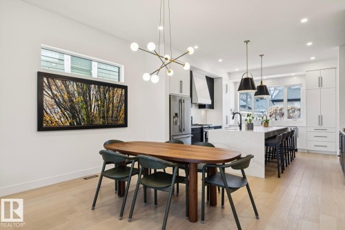 Open concept living area with light wood flooring, a modern chandelier, and a white kitchen featuring a large island with seating, pendant lighting, and stainless steel appliances - 11146 62 Street Nw, Edmonton, AB - Indoor Photo Showing Dining Room