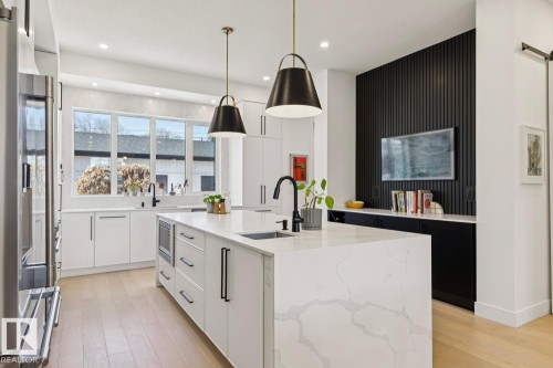 The kitchen features white cabinetry, a large center island with a white countertop, and light wood flooring - 11146 62 Street Nw, Edmonton, AB - Indoor Photo Showing Kitchen With Upgraded Kitchen