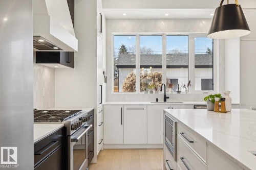 The kitchen features a gas range with an overhead vent, white cabinetry, and a large window above the sink - 11146 62 Street Nw, Edmonton, AB - Indoor Photo Showing Kitchen With Upgraded Kitchen