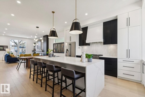 The kitchen features an expansive island with a waterfall countertop, pendant lighting, and a white and black color scheme - 11146 62 Street Nw, Edmonton, AB - Indoor Photo Showing Kitchen With Upgraded Kitchen