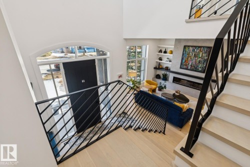 The property features a staircase with light-toned wooden steps and black metal railings, leading down to a living area with a fireplace and built-in shelving - 11146 62 Street Nw, Edmonton, AB - Indoor