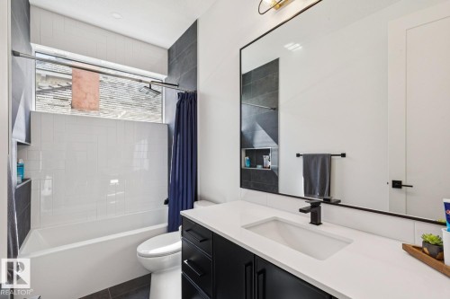 This bathroom features a full-sized bathtub with white subway tile surround, a built-in shower niche, and a contemporary vanity with a white countertop and black cabinetry - 11146 62 Street Nw, Edmonton, AB - Indoor Photo Showing Bathroom