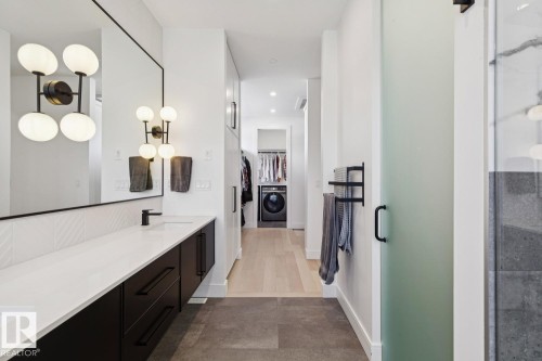 Bathroom featuring a spacious double vanity with a white countertop and dark cabinetry, a large mirror, and modern light fixtures - 11146 62 Street Nw, Edmonton, AB - Indoor