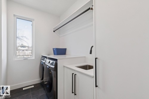 This laundry room features dark tiled flooring, a window, and a built-in sink with a modern faucet - 11146 62 Street Nw, Edmonton, AB - Indoor Photo Showing Laundry Room