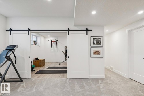 The property features a dedicated workout space with a window, light wood flooring, and track lighting, separated by white barn doors with black hardware - 11146 62 Street Nw, Edmonton, AB - Indoor